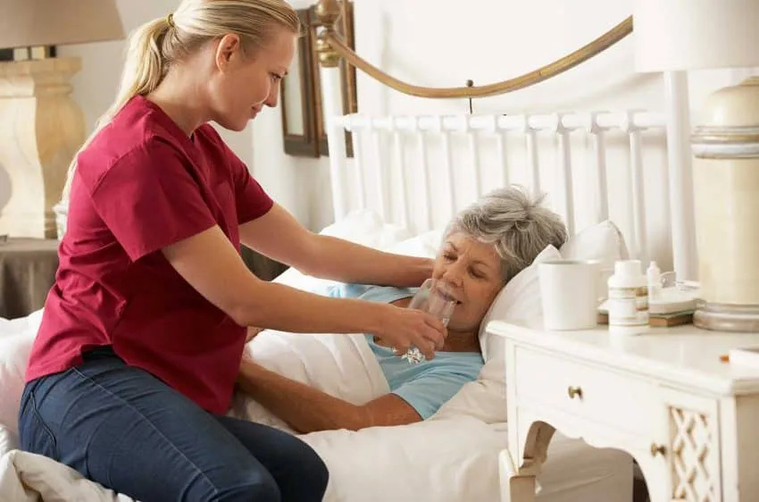 Intervenante qui aide une dame âgée à boire, au lit